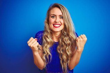 Genç güzel kadın mavi izole arka plan üzerinde duran sürpriz kutluyor ve kollarını kaldırdı ve açık gözleri ile başarı için şaşırttı. Kazanan kavramı.