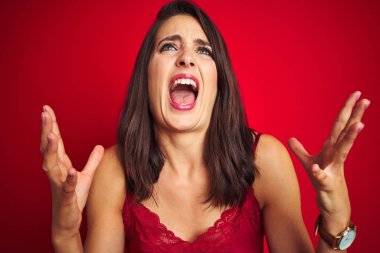 Genç güzel kadın kırmızı izole arka plan deli ve deli bağırarak üzerinde seksi iç çamaşırı giyen ve agresif ifade ve kollar kaldırdı ile bağırıyor. Hayal kırıklığı kavramı.