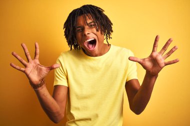 Dreadlocks ile rahat t-shirt giyen afro adam izole sarı arka plan üzerinde duran deli kutluyor ve silah kaldırdı ve açık gözleri ile başarı için hayran heyecanlı çığlık. Kazanan kavramı