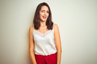 Genç güzel kadın beyaz izole arka plan üzerinde duran t-shirt giyen seksi ifade, neşeli ve mutlu yüz ile kameraya bakarak göz kırpıyor.