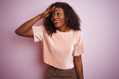 Genç afro-amerikan kadın izole pembe arka plan üzerinde duran t-shirt giyen çok mutlu ve başının üzerinde el ile uzak görünümlü gülümsüyor. Arama konsepti.