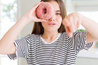 Güzel genç kız çocuk kamera ve size parmak ile işaret tatlı pembe donut yeme, el işareti, önden olumlu ve kendinden emin jest