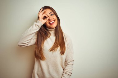 İzole beyaz arka plan üzerinde kış boğazlı kazak giyen genç güzel kadın el gülümseyerek ok jest yapıyor, mutlu yüz ile parmaklardan bakan göz.