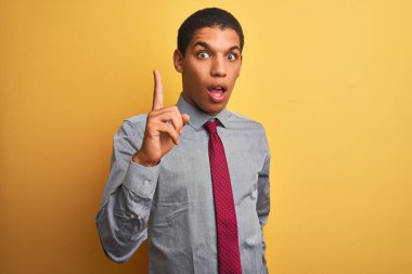 Genç yakışıklı Arap işadamı gömlek giyen ve izole sarı arka plan üzerinde kravat başarılı bir fikir ile parmak işaret. Çıktı ve mutlu. Bir numara.