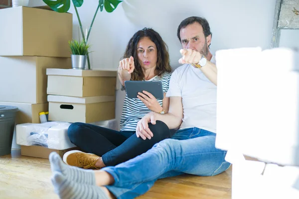 Orta yaş yaşlı çift kamera ve size parmak ile işaret tablet kullanarak yeni bir eve hareket, el işareti, önden olumlu ve kendinden emin jest