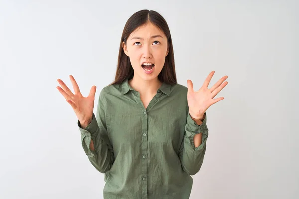 カジュアルな緑色のシャツを着た若い中国人女性は 孤立した白い背景の上に立って狂気と怒鳴り 攻撃的な表情と腕を上げて叫びました 欲求不満の概念 — ストック写真