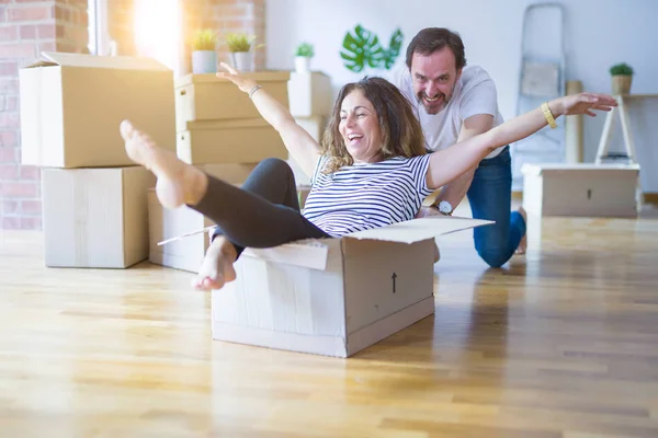 Middle age senior romantic couple having fun riding inside of cardboard, excited and smiling happy for moving to a new home