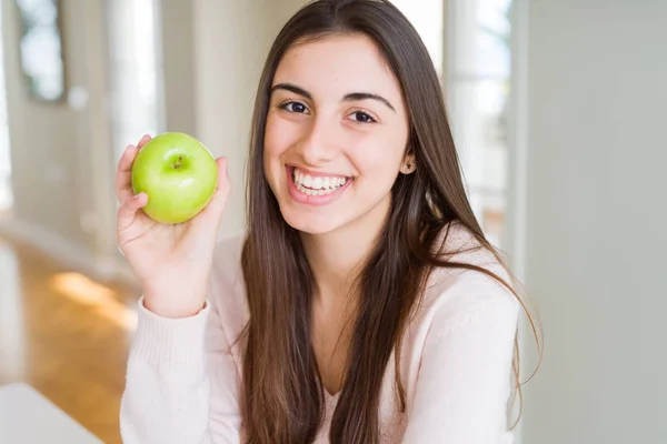 幸せな顔で健康的な緑のリンゴの果実を食べている美しい若い女性は 歯を見せる自信のある笑顔で立ち 微笑んでいます — ストック写真