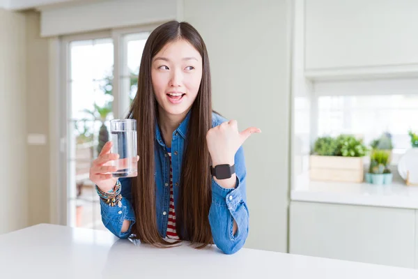 美丽的亚洲女人喝着一杯淡水指着 用大拇指向一边露出开心的脸微笑 — 图库照片