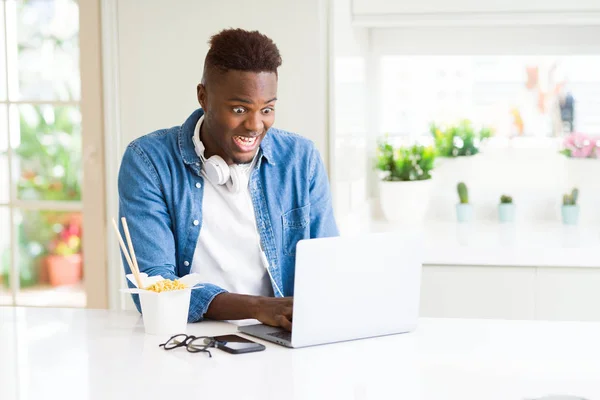笑みを浮かべて麺を楽しむハンサムな若いアフリカ ビジネス男配信アジアの食べ物を食べると コンピューターを使用しての作業 — ストック写真