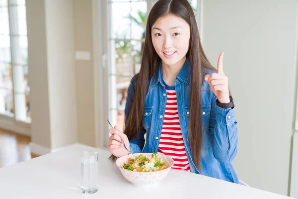 健康的なパスタサラダを食べる美しいアジアの女性は 幸せな顔で指を指すアイデアや質問に驚き ナンバーワン — ストック写真