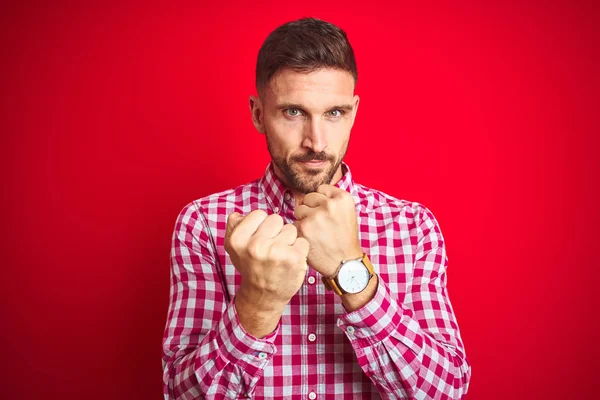 Kırmızı izole arka plan üzerinde genç yakışıklı adam yumruk savunma jesti ile mücadele etmeye hazır, kızgın ve üzgün yüz, sorun korkuyor