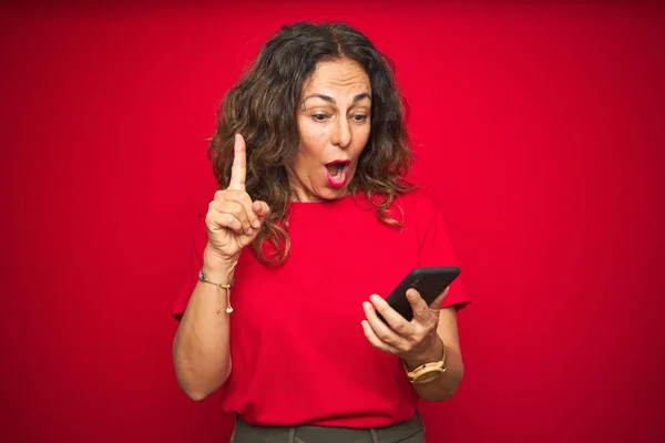 Seniorin Mittleren Alters Mit Smartphone Über Rotem Isoliertem Hintergrund Überrascht — Stockfoto