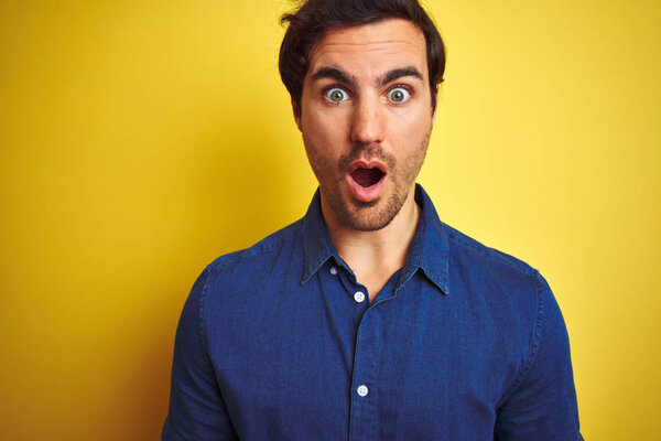 Молодой красивый мужчина с татуировкой в повседневной рубашке стоит на изолированном желтом фоне испуганный в шоке с неожиданным лицом, напуганный и взволнованный выражением страха
