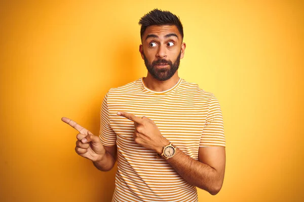 年轻的印度男子穿着T恤站在孤立的黄色背景 指着一边担心和紧张用双手 关切和惊讶的表情 — 图库照片