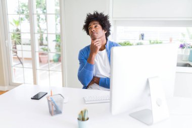 Afro-Amerikan adam çene üzerinde el ile bilgisayar kullanarak çalışan soru, dalgın ifade hakkında düşünme. Düşünceli bir yüzle gülümsüyor. Şüphe kavramı.