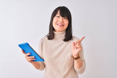 Izole beyaz arka plan üzerinde duran mavi tablet kullanarak güzel Çinli kadın çok mutlu yan el ve parmak ile işaret
