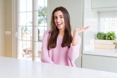 Pembe kazak giyen güzel genç kadın gülümseyerek neşeli sunum ve avuç içi kameraya bakarak işaret.