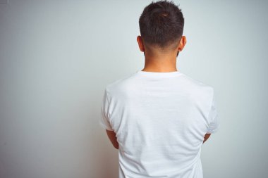 İzole beyaz arka plan üzerinde duran t-shirt giyen genç hintli adam çapraz kolları ile geriye bakarak ayakta