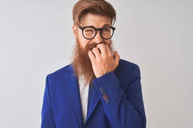 Genç kızıl İrlandalı işadamı takım elbise ve gözlük giyen izole beyaz arka plan görünümlü stresli ve ağız tırnak ısırma elleri ile sinir. Anksiyete sorunu.