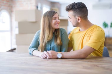 Evde masada oturan genç güzel çift, onların arkasında karton kutular ile yeni eve hareket için çok mutlu aşık sarılmak