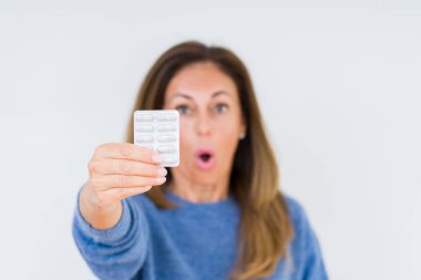 Izole arka plan üzerinde ilaç hapları tutan orta yaşlı kadın sürpriz bir yüz ile şok korkmuş, korku ifade korku ve heyecanlı