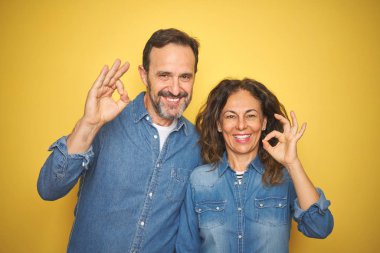 Güzel orta yaş çift birlikte izole sarı arka plan üzerinde duran olumlu el ve parmaklar ile ok işareti yapıyor gülümseyerek. Başarılı ifade.