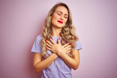 Pembe izole arka plan üzerinde duran mor t-shirt giyen genç güzel kadın kapalı gözleri ve yüzünde minnettar jest ile göğüs üzerinde gülümseyerek. Sağlık kavramı.