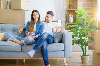 Genç çift yeni bir ev, yeni bir daire taşımak için mutlu gülümseyen bir fincan kahve içerken kanepede oturan rahatlatıcı hareket