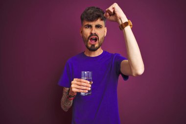 Dövme içme cam su izole mor arka plan üzerinde duran kızgın ve öfke ile bağırarak sinirli, deli ve yükseltilmiş el, öfke kavramı ile bağırıyor