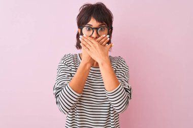 İzole pembe arka plan üzerinde çizgili t-shirt ve gözlük giyen genç güzel kadın hata için elleri ile ağız kapsayan şok. Gizli kavram.