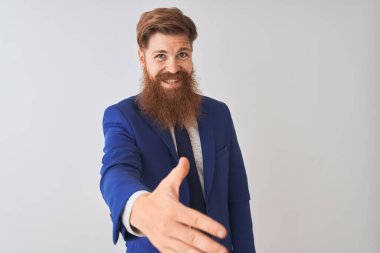 Genç kızıl saçlı İrlandalı işadamı takım elbise giyen izole beyaz arka plan üzerinde ayakta selamlama ve karşılama olarak dostça sunan samimi gülümseyerek. Başarılı iş.
