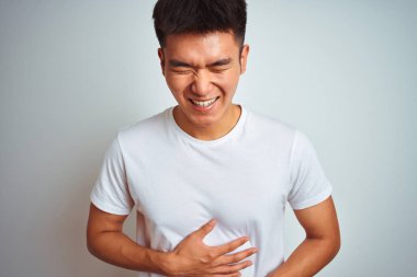 Genç asyalı Çinli adam izole beyaz arka plan üzerinde duran t-shirt giyen gülümseyerek ve yüksek sesle sert gülüyor çünkü vücut elleri ile komik çılgın şaka.