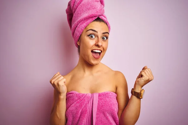 Young beautiful woman wearing towel after shower over isolated pink background celebrating surprised and amazed for success with arms raised and open eyes. Winner concept.