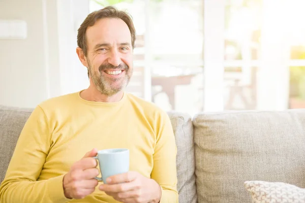 ハンサムな中年男がソファーに座ってリラックス コーヒーを一杯飲み 自宅のカメラで笑顔 — ストック写真