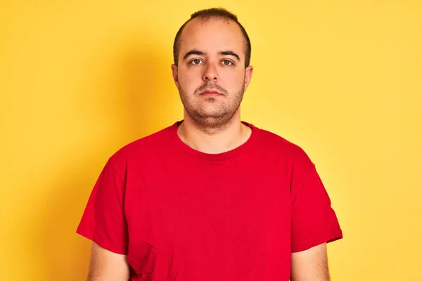 真面目に考えるスマートな顔に自信のある表情で孤立した黄色の背景の上に立つ赤いカジュアルなTシャツを着た若者 — ストック写真