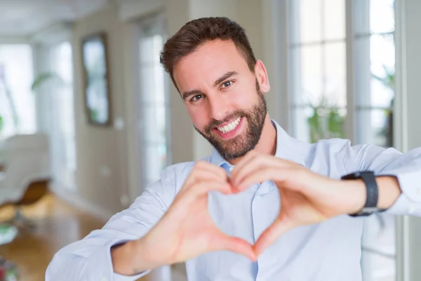 Handsome business man smiling in love showing heart symbol and shape with hands. Romantic concept.