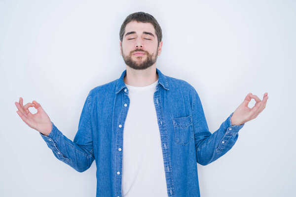 Young handsome hispanic man wearing denim jacket over white isolated background relax and smiling with eyes closed doing meditation gesture with fingers. Yoga concept.
