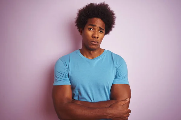African american man with afro hair wearing blue t-shirt standing over isolated pink background skeptic and nervous, disapproving expression on face with crossed arms. Negative person.