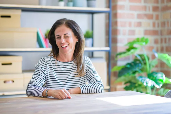 Orta yaş yaşlı kadın evde masada oturan seksi ifade, neşeli ve mutlu yüz ile kameraya bakarak göz kırpıyor.