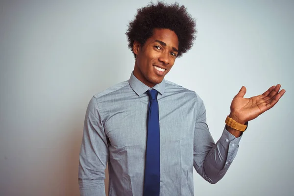 American business man with afro hair wearing shirt and tie over isolated white background smiling cheerful presenting and pointing with palm of hand looking at the camera.