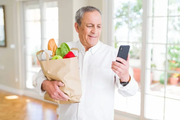 Handsome senior man holding paper bag full of fresh groceries an