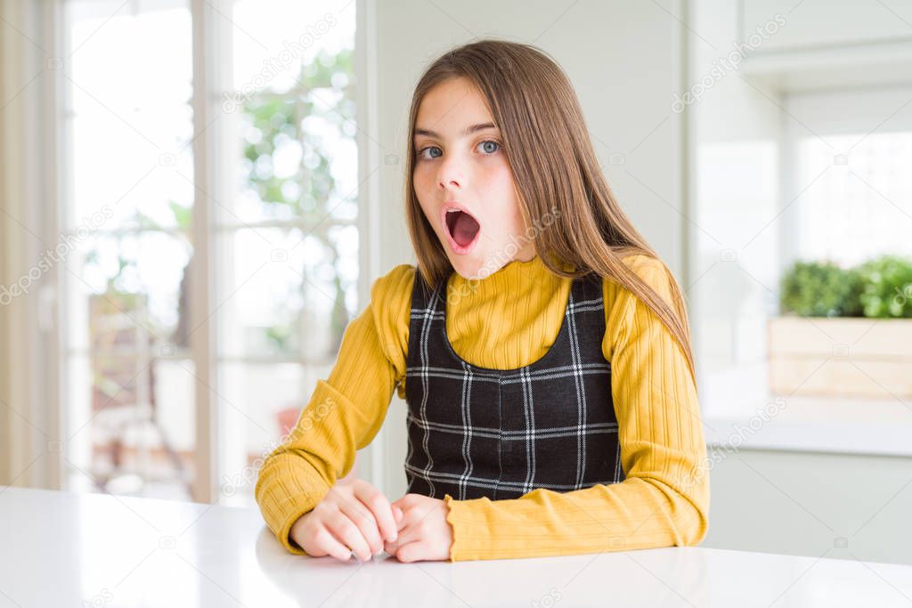 Young beautiful blonde kid girl wearing casual yellow sweater at home In shock face, looking skeptical and sarcastic, surprised with open mouth