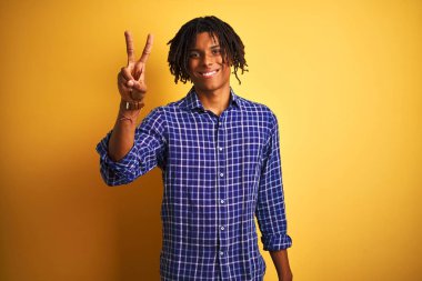 Kendinden emin ve mutlu gülümserken izole sarı arka plan üzerinde duran ve parmakları ile işaret eden rahat gömlek giyen dreadlocks ile Afro adam.