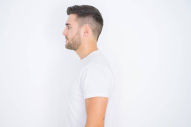 Genç yakışıklı adam yan bakarak beyaz izole arka plan üzerinde rahat beyaz t-shirt giyen, kendine güvenen gülümseme ile doğal yüz ile profil poz rahat.