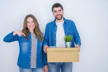 Genç çift kendini parmak işaret sürpriz yüz ile beyaz izole arka plan üzerinde yeni bir eve hareket karton kutu tutan