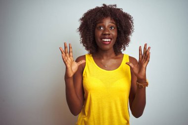 Genç afrikalı afro kadın izole beyaz arka plan üzerinde sarı t-shirt giyen deli ve deli bağırarak ve agresif ifade ve kollar kaldırdı ile bağırıyor. Hayal kırıklığı kavramı.