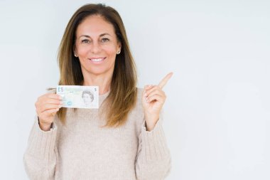 Orta yaş kadın izole arka plan üzerinde 5 lira banka notu tutan çok mutlu yan el ve parmak ile işaret