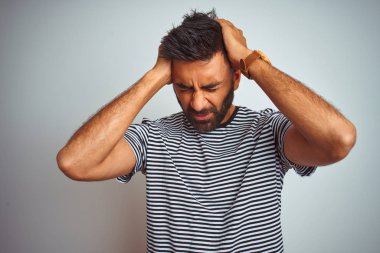 Siyah çizgili t-shirt giyen genç hintli adam izole beyaz arka plan üzerinde baş ağrısı umutsuz acı ve stresli çünkü ağrı ve migren. Eller baş üstünde.