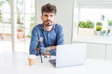 Genç adam mikrofon ve dizüstü bilgisayar şüpheci ve sinir kullanarak podcast kayıt, çapraz kolları ile yüzünde ifade onaylamayan. Negatif kişi.